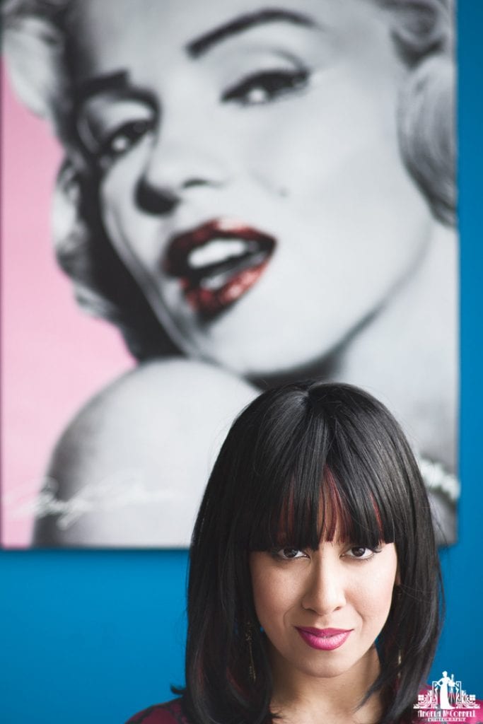 Portrait of a woman looking at the camera with an Andy Warhol reproduction Marilyn Monroe picture in the background