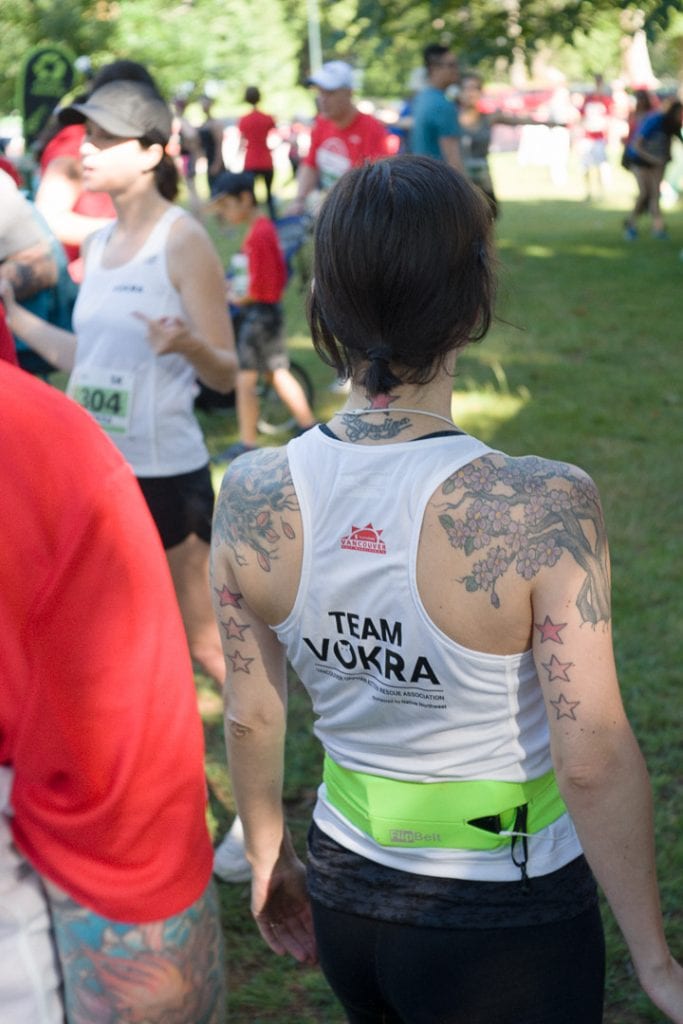 Tattooed woman wearing a Team VOKRA tank top stretching before a run