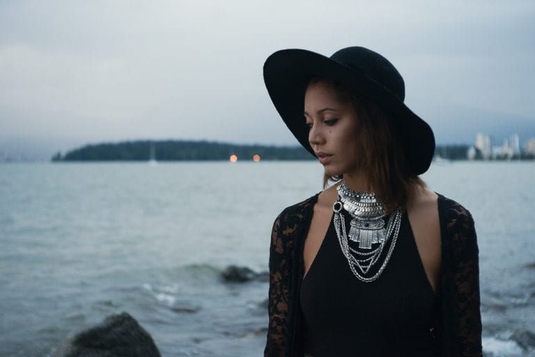 Natural light portrait of a young woman in a black hat and silver necklaces with English Bay and Stanley Park in the distance