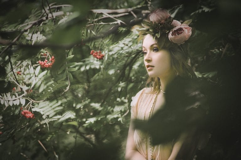 Natural light portrait of a young woman wearing a flower crown framed by leaves in a wooded area