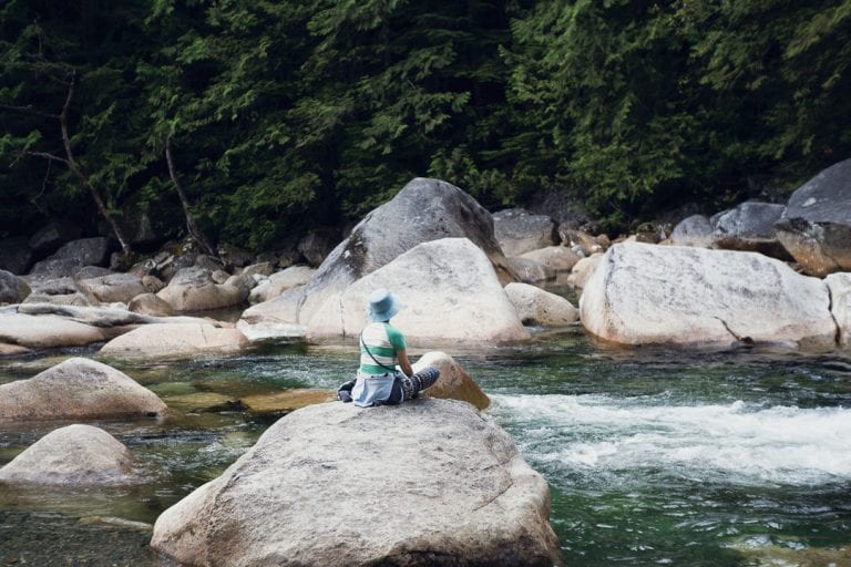 Image of a woman sitting on a boulder overlooking a river and waterfall at Golden Ears Provincial Park