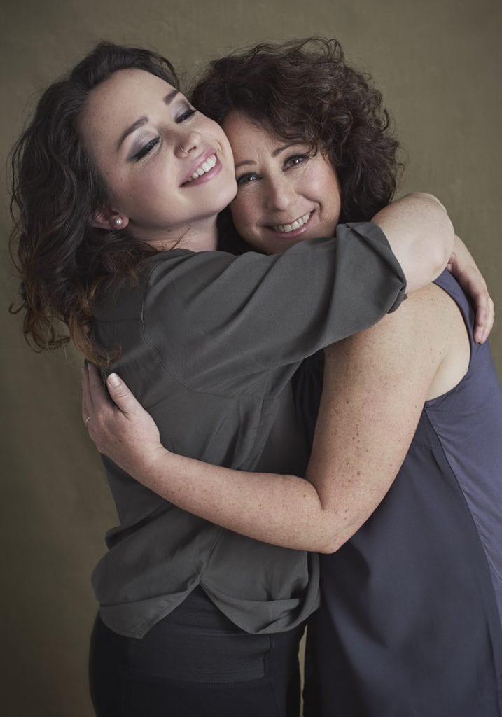 Studio portrait of a young woman smiling broadly with closed eyes bear hugging her mother who is smiling at the camera for portraits with Mum by Vancouver contemporary portrait photographer Angela McConnell