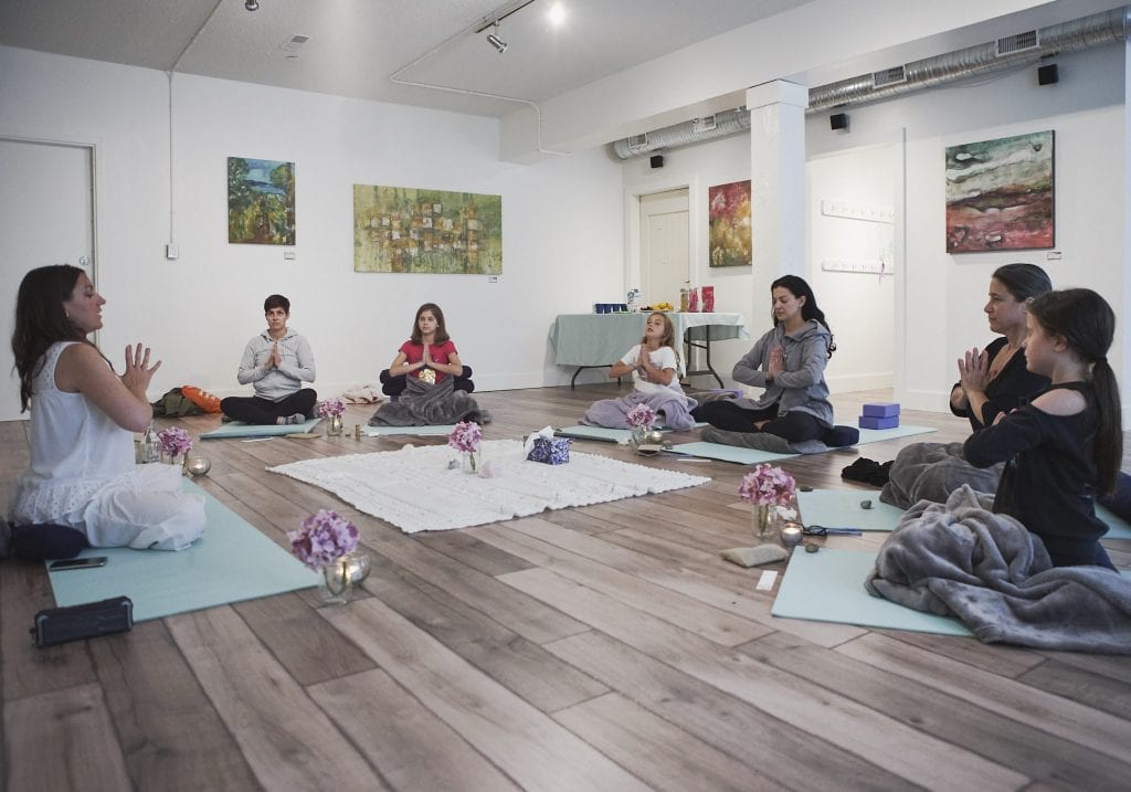 A group of women and their young daughters sit on yoga mats in front of a facilitator during a yoga exercise at a mother and daughter workshop by Vancouver workshop and retreat photographer Angela McC