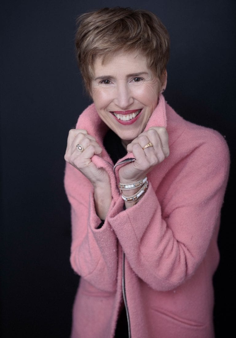 Older woman wearing a pink coat smiles during a portrait session by Vancouver contemporary portrait photographer Angela McConnell